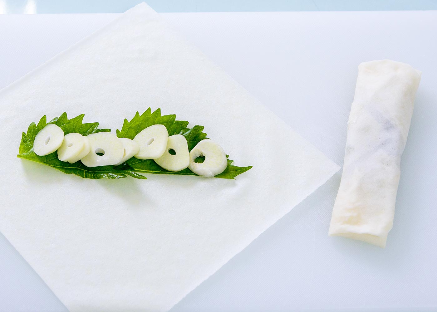 まな板に春巻きの皮を１枚のせ、左右と上方に糊を塗る。中央に青じそ２枚を横に並べ、にんにくのスライスをのせ、手前の皮を折って重ね、左右を重ねて巻いて留める。